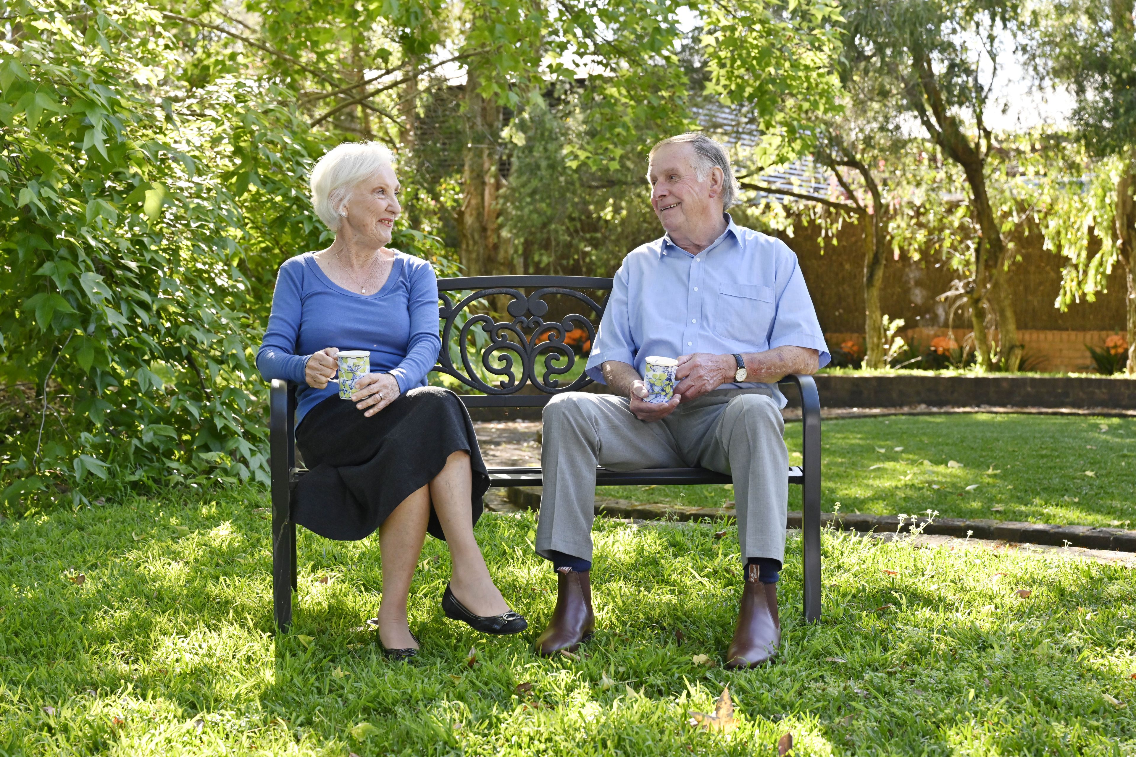 Elderly couple sitting on a park bench looking at each other