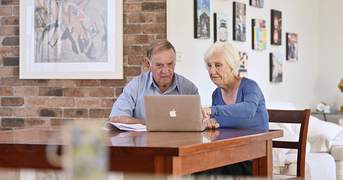 An older couple research together on their laptop.